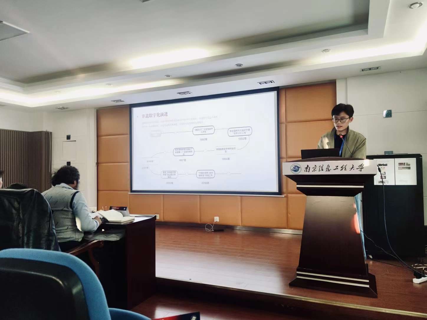 A presenter discussing research beside a projected slide.